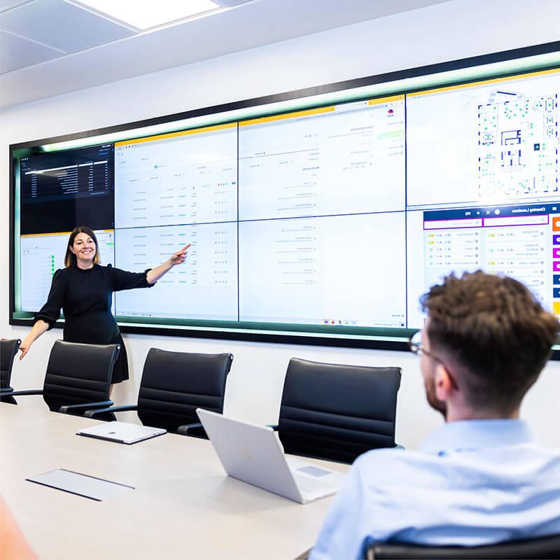 A woman pointing at various charts on a screen in boardroom